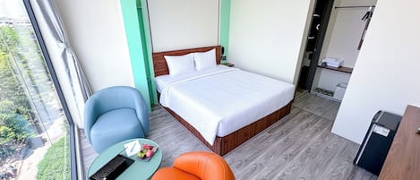 Habitación de hotel con cama, escritorio, silla, una mesita con un ordenador portátil y vistas al exterior con vegetación.