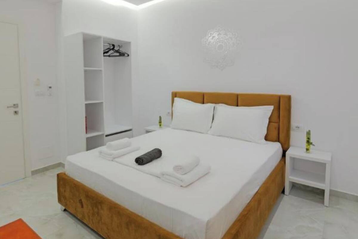 A modern bedroom with a large bed, wooden headboard, white bedding, a small bedside table, and a built-in wardrobe with a clothing rack.
