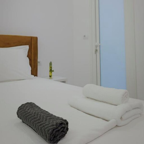 A neatly made bed with white linens and a grey textured blanket, a white pillow, and a small bedside table with a bottle.