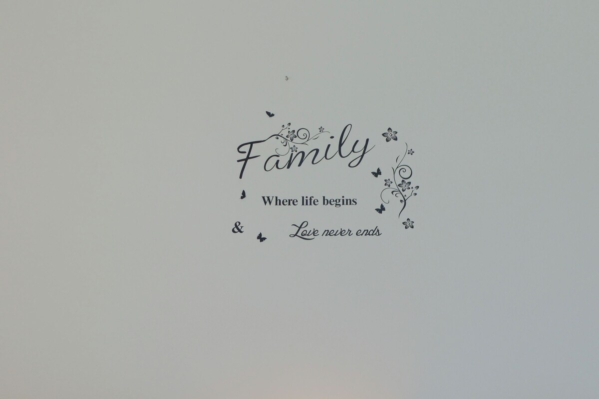 A room with two wooden beds, a nightstand with a lamp, and a wall decal with the word 'Family' and a quote.