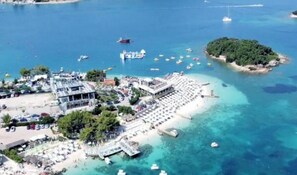 An aerial view of a coastal area with a beach, a marina, and a small island. - Central Garden Sofia Apartments & Studios (Ksamil)