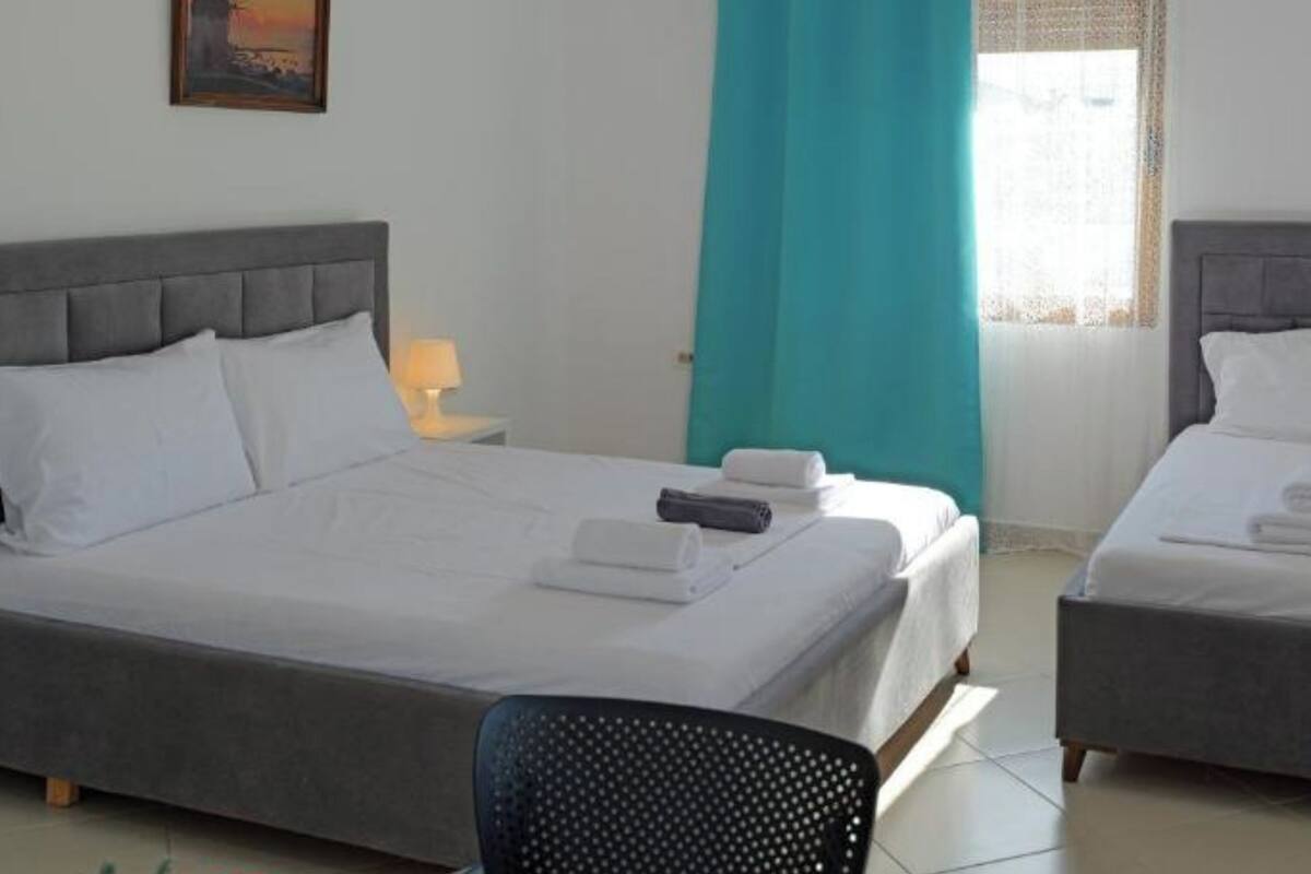 A hotel room with a large bed, a smaller bed, a chair, a painting on the wall, and a window with curtains.
