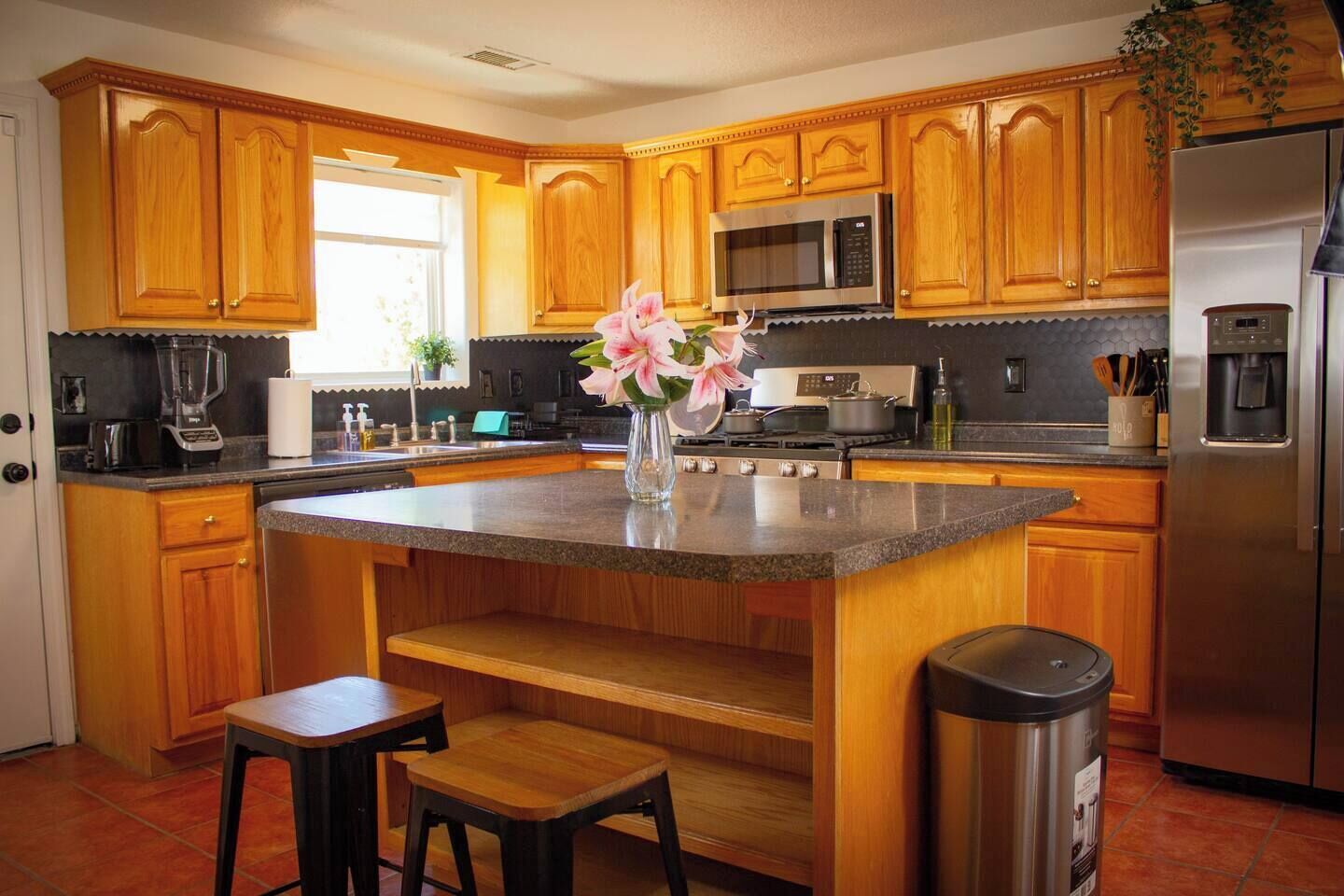 Una cocina con armarios de madera, encimera de granito, refrigerador de acero inoxidable y un fregadero.