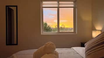 Un dormitorio con cama, ventana con vistas al atardecer y espejo montado en la pared.