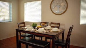 A dining room with a wooden table set for four, surrounded by chairs. There is a potted plant on the table, and a decorative tree wall art piece above it. - Azul Oasis - No house guest without prior approval from host. (Albuquerque)