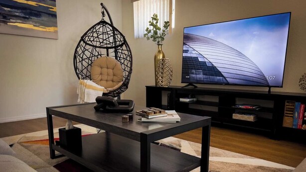 A modern living room with a dark wooden coffee table, a hanging chair, a flat-screen TV, and a bookshelf. - Azul Oasis - No house guest without prior approval from host. (Albuquerque)