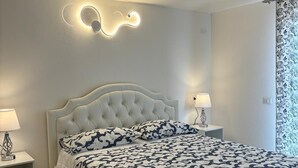 Une chambre à coucher avec une tête de lit capitonnée, une couvre-lit à motifs, des lampes de chevet et un luminaire fixé au mur.