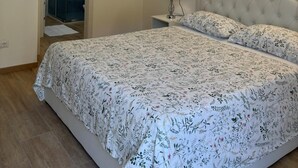 Une chambre à coucher comprenant un lit, une table de chevet, une lampe fixée au mur et une porte donnant sur une salle de bain.