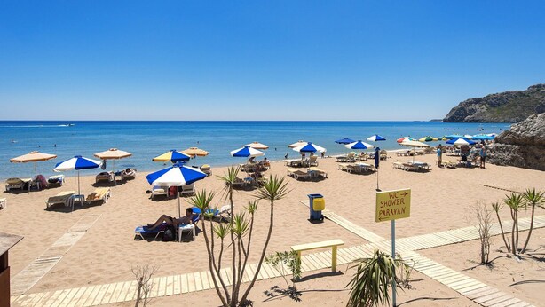 A beach with sun loungers, umbrellas, and a sign for a shower and toilet.