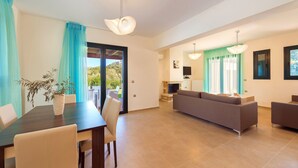 A modern living room with a sofa, a dining table with chairs, and a TV.