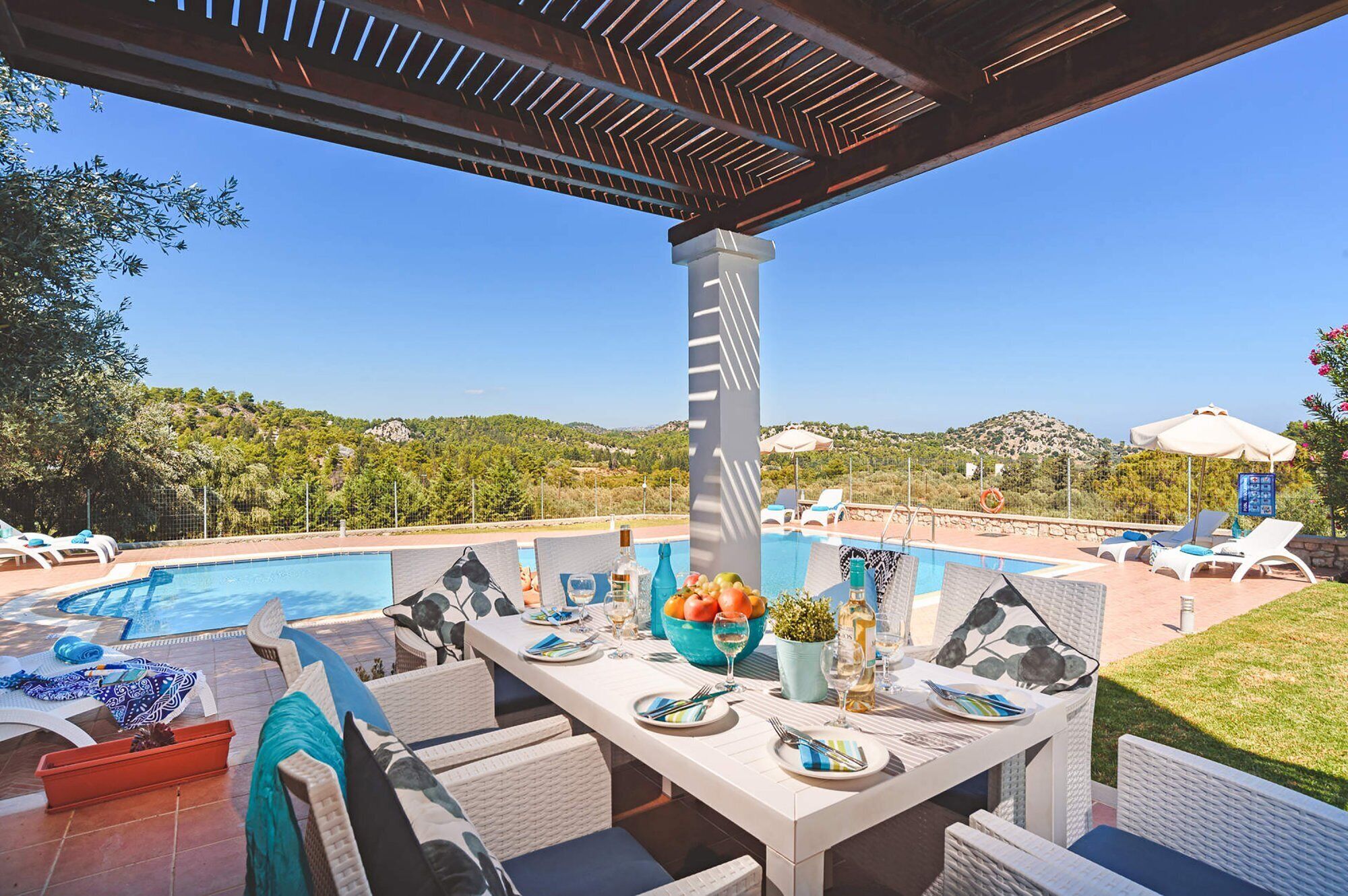 Uma área de piscina ao ar livre com espreguiçadeiras, uma mesa de jantar para dois e vista para a paisagem circundante.