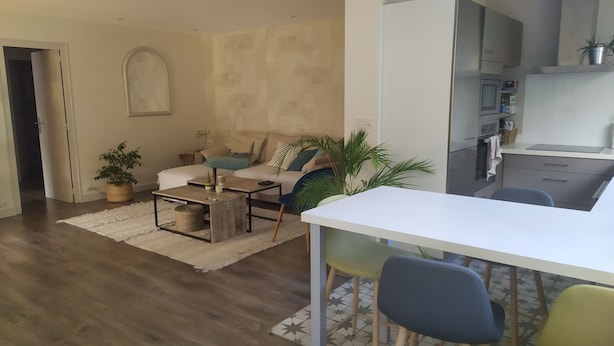 Una sala de estar con sofá, mesa de centro y sillas, una cocina con electrodomésticos modernos, y un comedor con mesa y sillas blancas.