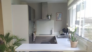 Cocina moderna con una isla central, dos sillas, una planta en maceta y una ventana con cortinas.