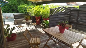 Un patio exterior con mobiliario de madera, plantas en macetas y un cerco de madera.