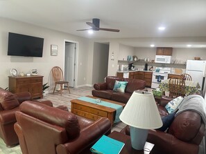 Uma sala de estar com um sofá de couro marrom, um armário de madeira, uma televisão e um ventilador de teto.