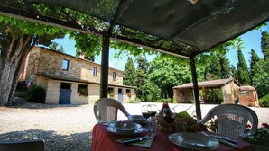 An outdoor dining area with a table set for two, surrounded by trees and stone buildings. - Agriturismo Bellavista (Radicondoli)