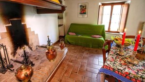 A cozy room with a green sofa, a table with candles, and a fireplace with copper pots. - Agriturismo Bellavista (Radicondoli)