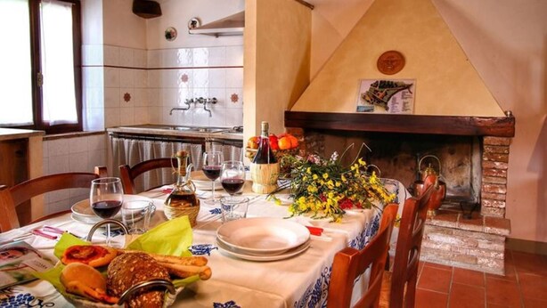 Une table à manger dressée avec des assiettes, des verres et une bouteille de vin, avec une cheminée et un mur recouvert de carreaux en arrière-plan.