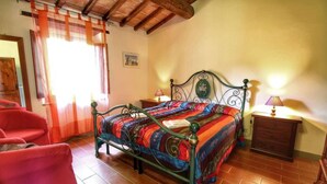 Une chambre à coucher avec un lit en métal, une courtepointe aux couleurs vives, une table de chevet en bois et une chaise rouge.