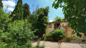 Un bâtiment rustique à la façade en pierre, entouré d’une végétation luxuriante et de grands arbres.