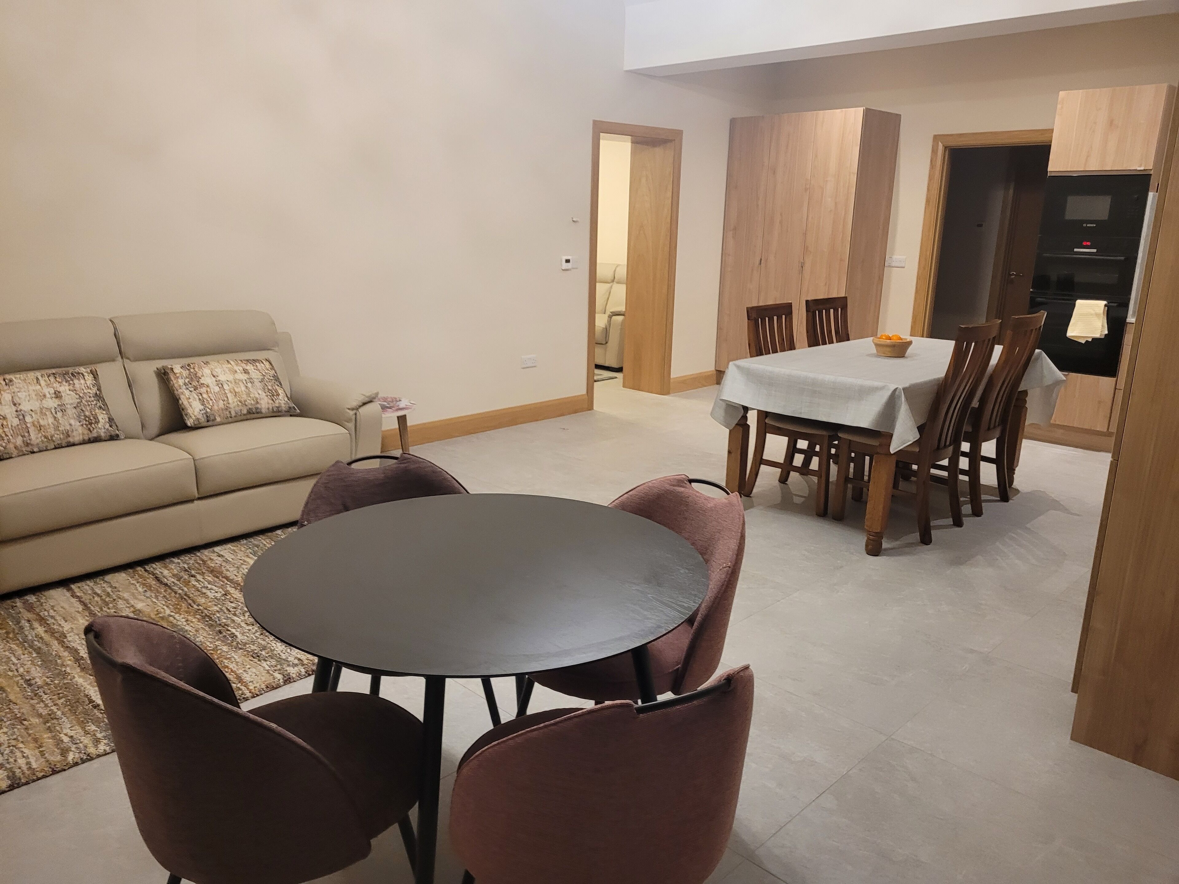 A living room with a sofa, a round table, and chairs. There is a dining area with a table and chairs.