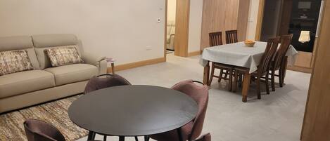 A living room with a sofa, a round table, and chairs. There is a dining area with a table and chairs.