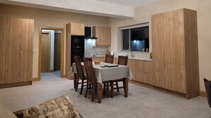 A modern kitchen with wooden cabinets, a dining area with a table and chairs, and a ceiling light fixture. - Immaculate 2-bed Cottage in Tuam (Polladooey)