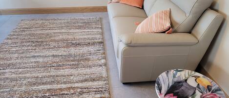 A living room with a beige sofa, a patterned rug, and a small table with a floral print.