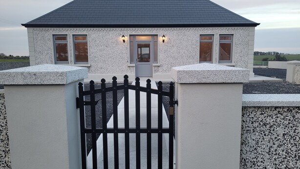 A house with a gated entrance, a sloped roof, and a small porch with a door. - Immaculate 2-bed Cottage in Tuam (Polladooey)