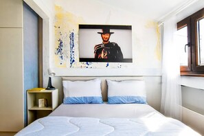 Una camera da letto con un letto, due cuscini, un comodino, una lampada e un quadro appeso al muro.