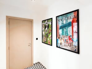 A hallway with two framed posters on the wall, a closed door, and a patterned rug on the floor.