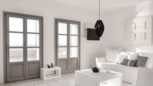 Ein modernes Wohnzimmer mit einem weißen Sofa, einem Couchtisch und einem Beistelltisch. Große Fenster bieten einen Ausblick ins Freie.