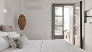 Ein Schlafzimmer mit Bett, Kissen, einer Hängeleuchte und einer offenen Tür zu einem Außenbereich.