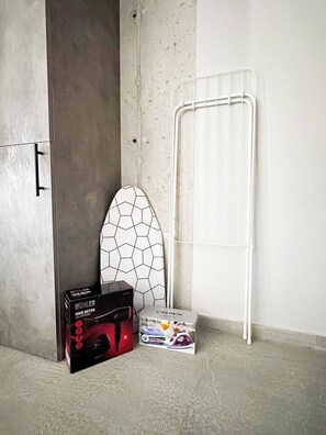 A room with a concrete wall, a white metal drying rack, a white hexagonal object, and two boxes labeled "MÜHLER HAIR DRYER WITH DIFFUSER" and "CROWN CS2015T."