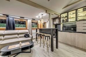 A modern kitchen with a dining area, featuring a sofa, stools, and a coffee table.