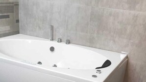 A modern bathroom with a white bathtub, grey tiled walls, and a grey floor. - A.V.N Homestay (Kodaikanal)
