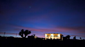 A two-story house with a flat roof and a balcony, surrounded by palm trees. - Tranquil 2-bedroom cabin in Yucca Valley with AC, WiFi (Yucca Valley)