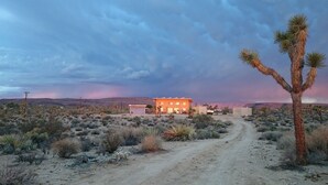 A desert landscape with a building featuring a garage and a dirt road leading to it. - Tranquil 2-bedroom cabin in Yucca Valley with AC, WiFi (Yucca Valley)