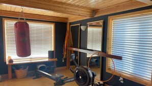 A home gym with a punching bag, exercise equipment, and large windows with blinds. - Tranquil 2-bedroom cabin in Yucca Valley with AC, WiFi (Yucca Valley)