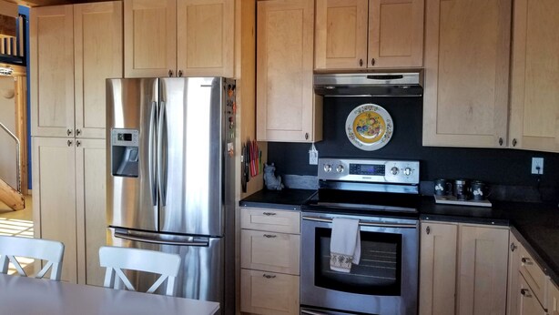 A modern kitchen with stainless steel appliances, wooden cabinets, and a dining area with a white table and chairs. - Tranquil 2-bedroom cabin in Yucca Valley with AC, WiFi (Yucca Valley)