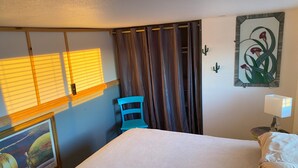 A hotel room with a bed, a chair, a painting, a window with blinds, and a wall-mounted cactus decoration. - Tranquil 2-bedroom cabin in Yucca Valley with AC, WiFi (Yucca Valley)