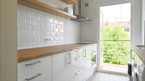 A modern kitchen with white cabinets, a wooden countertop, and a view of greenery outside.
