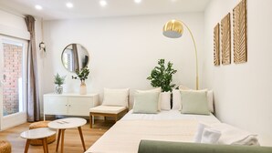 A modern bedroom with a large bed, bedside tables, a dresser, a mirror, and decorative plants.