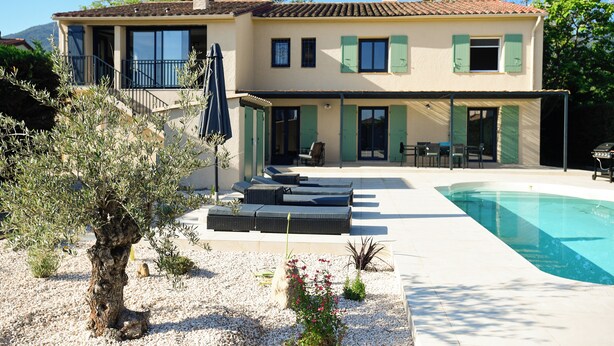A two-story house with a swimming pool, outdoor seating, and a garden with olive trees.