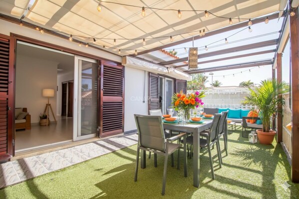 Une terrasse extérieure avec une table, des chaises et un pot de fleurs.