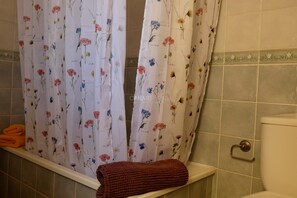 Un baño con cortinas de ducha con motivos florales, una bañera blanca, una toalla marrón y un inodoro con asa metálica.