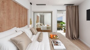 Ein modernes Hotelzimmer mit einem großen Bett, einem Nachttisch mit Obsttablett und Blick ins Freie.