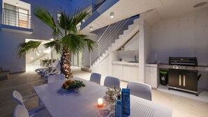 Eine moderne Küche mit Grill, ein Essbereich mit Tisch und Stühlen sowie eine Treppe zu einer oberen Ebene.