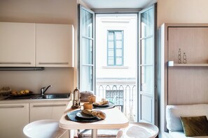 A compact kitchen with a dining area, a view of the outside balcony, and a small seating area with a sofa and cushions. - Del Pero Suite (Como)