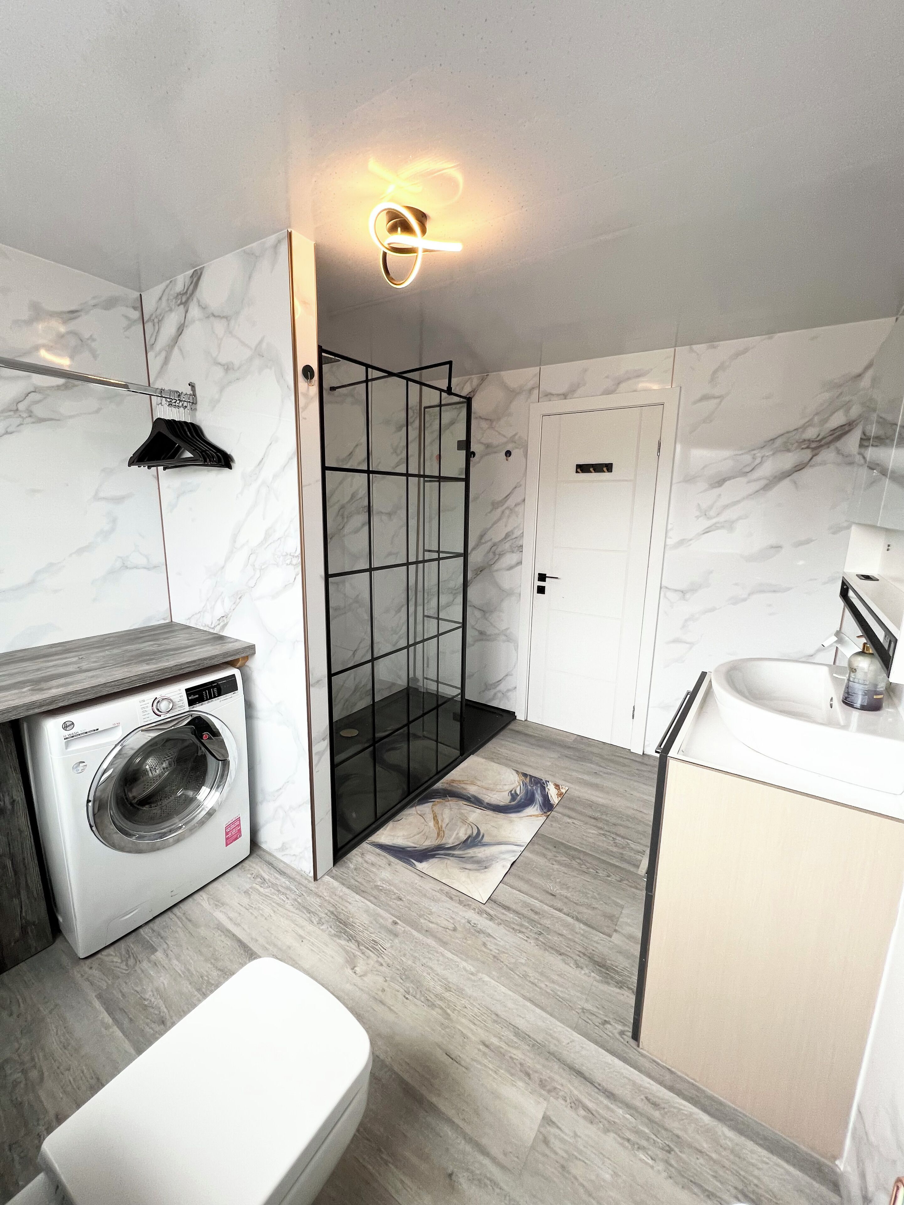 A modern bathroom with a built-in washing machine, a glass shower enclosure, and a sink with a mirror.